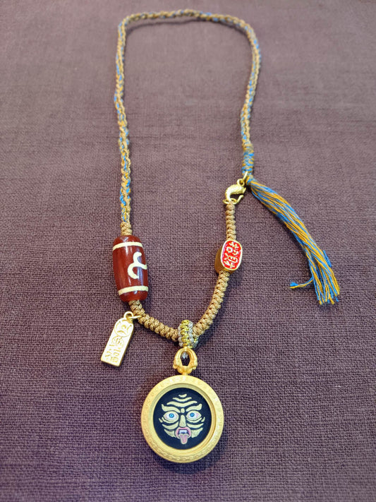 The Rekong Shridevi Thangka pendant with copper casing and Tibetan-style cord displayed as a sacred amulet for fortune and peace, embodying Buddhist tradition.