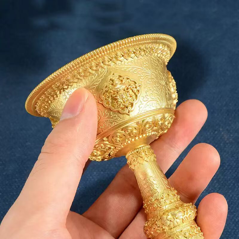 Tibetan Buddhist sacrificial implements culture: Detailed view of the Eight Auspicious Symbols (Ashtamangala) engraved on a gilded bronze ritual chalice for sacred offerings.