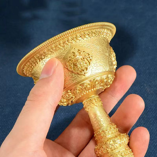 Tibetan Buddhist sacrificial implements culture: Detailed view of the Eight Auspicious Symbols (Ashtamangala) engraved on a gilded bronze ritual chalice for sacred offerings.