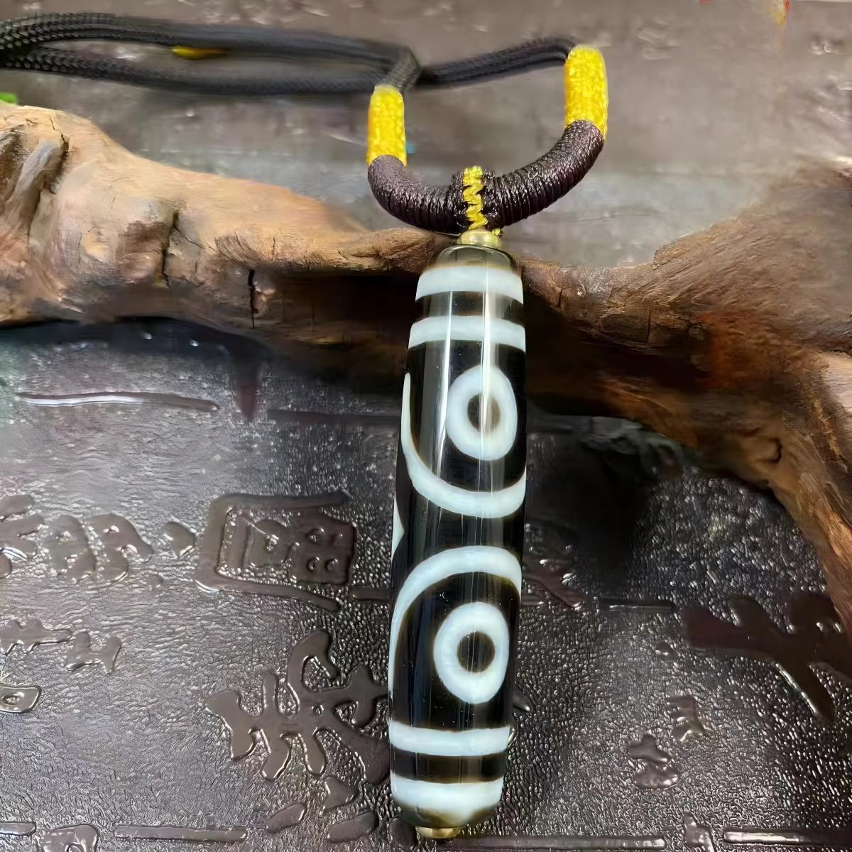 Natural Nine-Eye Dzi pendant on vertical thread, handcrafted Tibetan Buddhist jewelry culture piece, promoting luck, peace, and spiritual harmony.