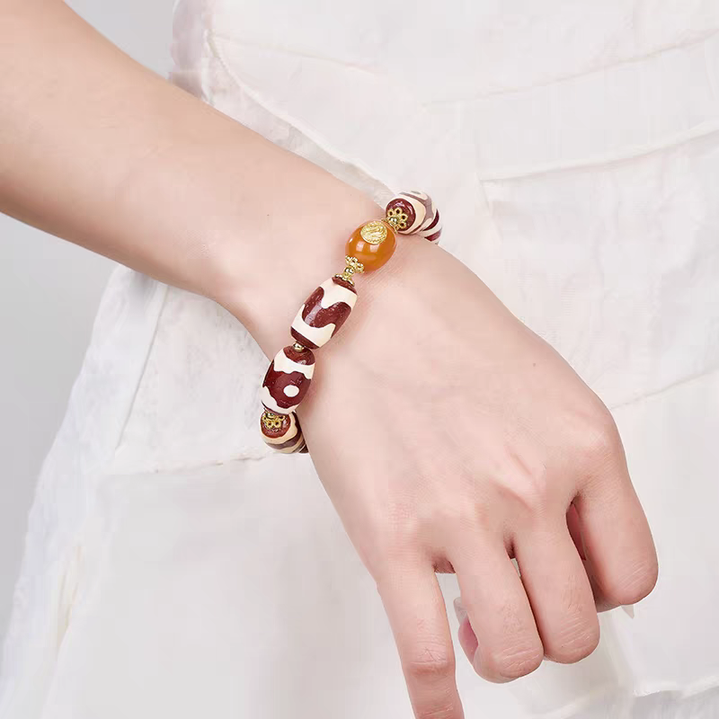  Handcrafted red Dzi bracelet featuring diverse sacred patterns, representing a blend of Buddhist sacrificial items art and ancient Tibetan Buddhist sacrificial implements culture.
