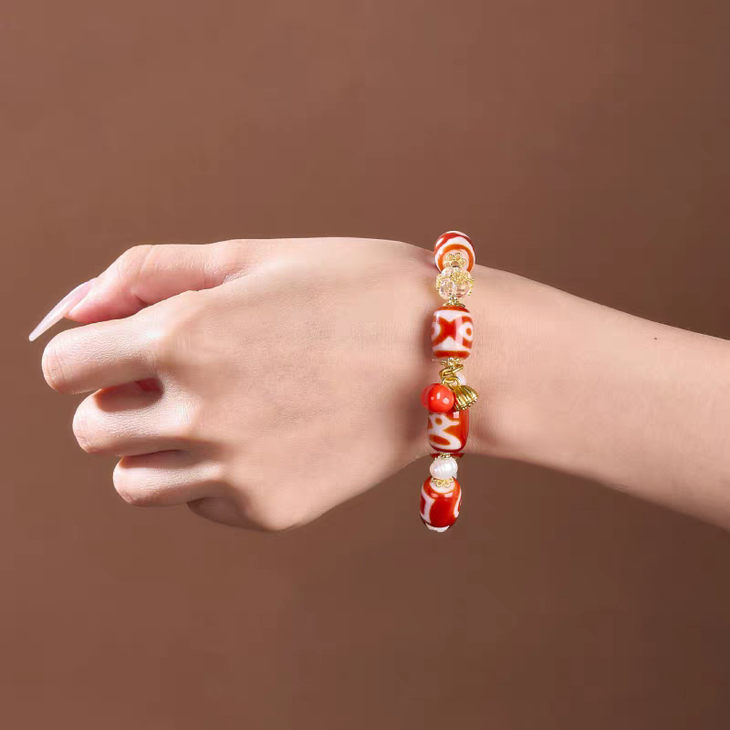 Handcrafted red Dzi bracelet with bucket beads representing wealth and stability in Buddhist sacrificial items art and ancient traditions.

