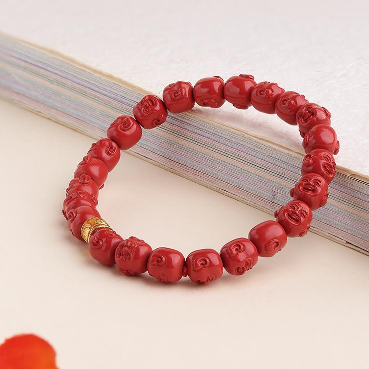 The deep red hue of hand-painted cinnabar beads and a Buddha charm in this Tibetan Buddhist bracelet. This meditative jewelry art piece is shown in a serene, natural setting.