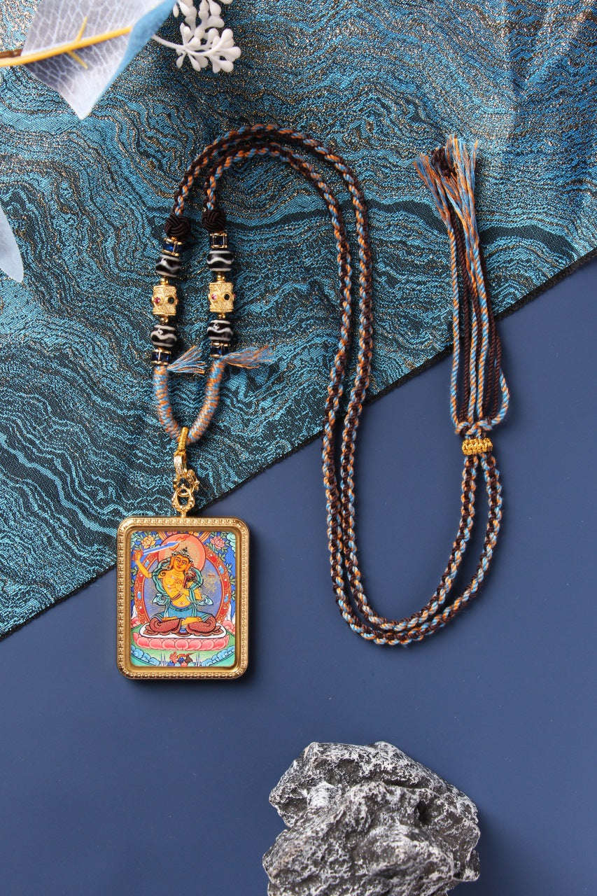 A 3.5x4.5cm hand-painted Rebgong Manjushri Thangka pendant with golden-orange complexion and flaming sword, set in a titanium steel frame.
