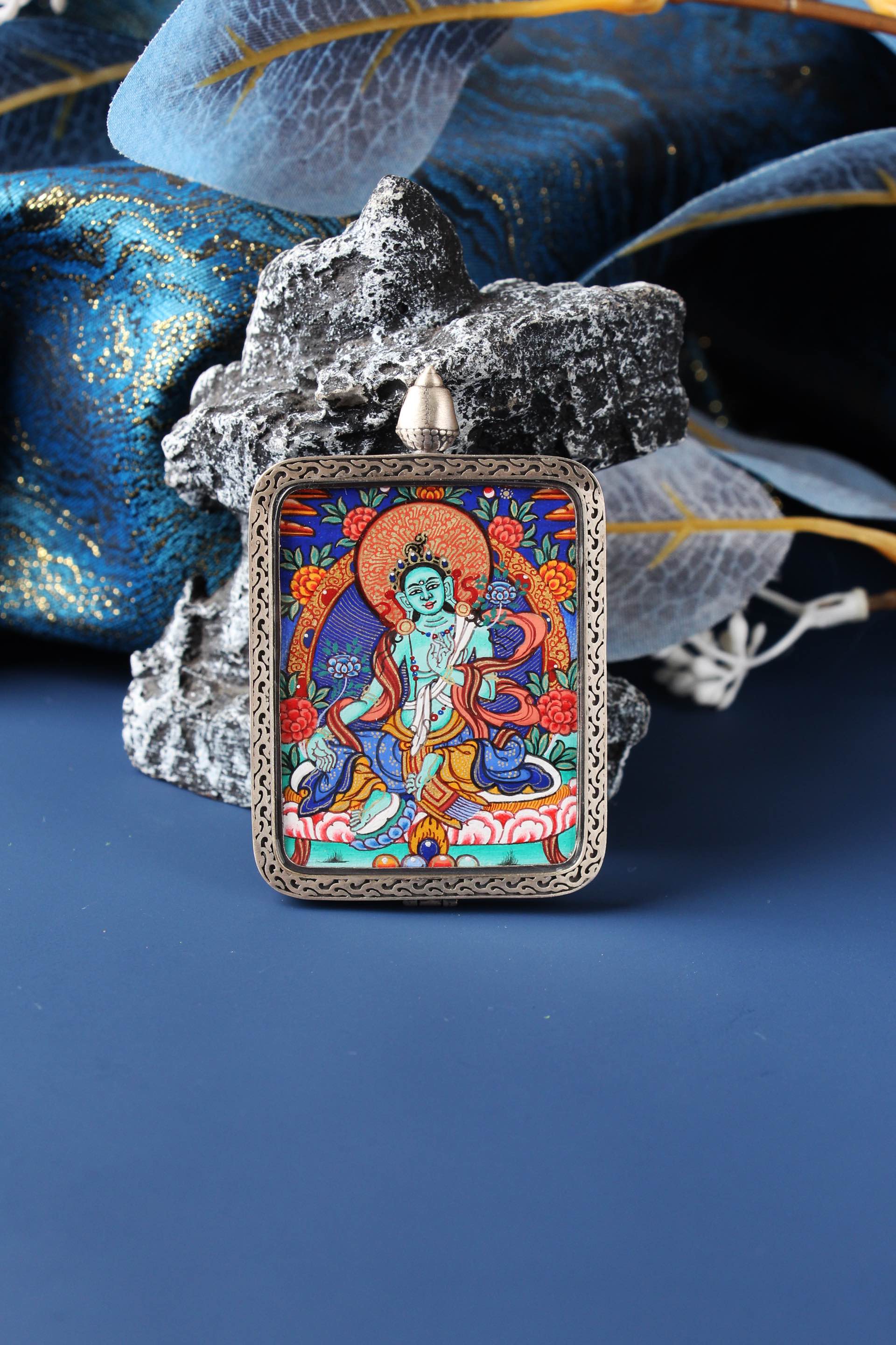 A 3.5x4.5cm hand-painted Green Tara Thangka from Rebgong, painted with natural mineral pigments by a Lama artist, in a silver protective frame.