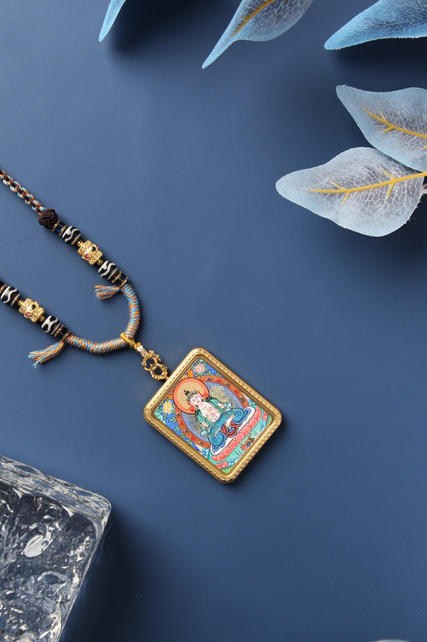 Close-up of a Rebgong Manjushri Thangka pendant featuring orange mineral pigments and intricate gold linework.