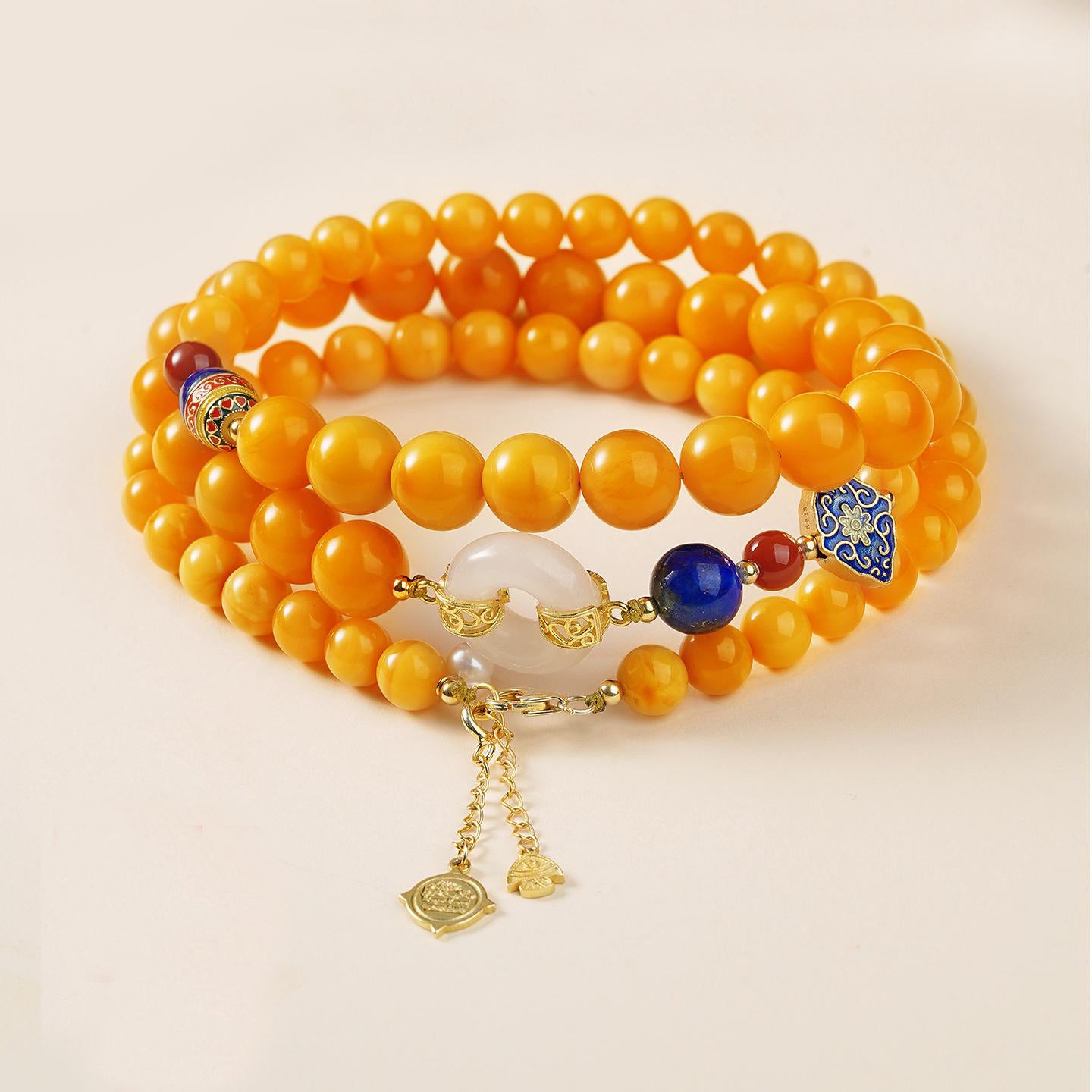 Mala-inspired amber necklace with lapis lazuli and silver charm, representing prosperity and protection.