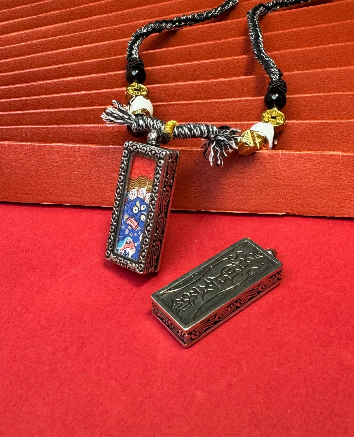 The Rekong Black Jambhala Thangka pendant with copper casing displayed as a sacred amulet for instant bestowal of wealth and relief from poverty, embodying Buddhist tradition.
