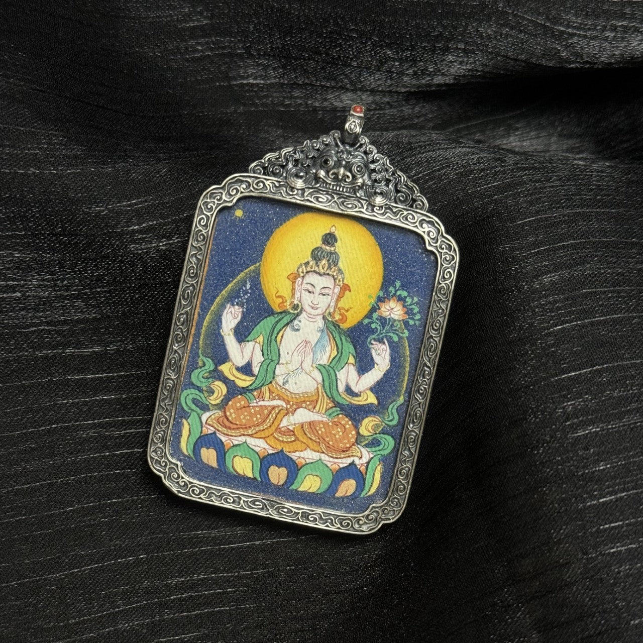  A 3.5x4.5cm hand-painted Bold-style Four-Armed Avalokiteshvara Thangka pendant featuring the embodiment of great compassion, encased in antique silver-tone metal, symbolising family peace and health in Tibetan Buddhist tradition.
