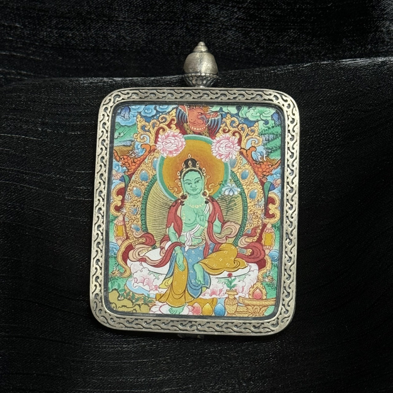 The Menri Green Tara Thangka pendant displayed as a sacred amulet for liberation and wisdom, embodying the compassion of the Liberator from Eight Fears in Tibetan Buddhist tradition.

