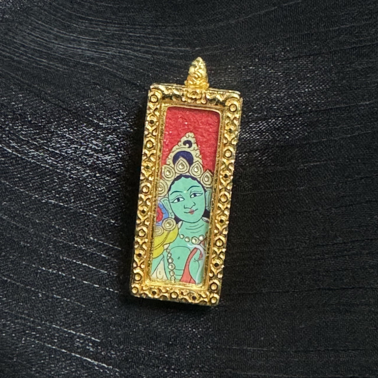 The Rebgong Buddha Head Green Tara Thangka pendant displayed as a sacred amulet for love, career and blessing, embodying Tibetan Buddhist tradition.

