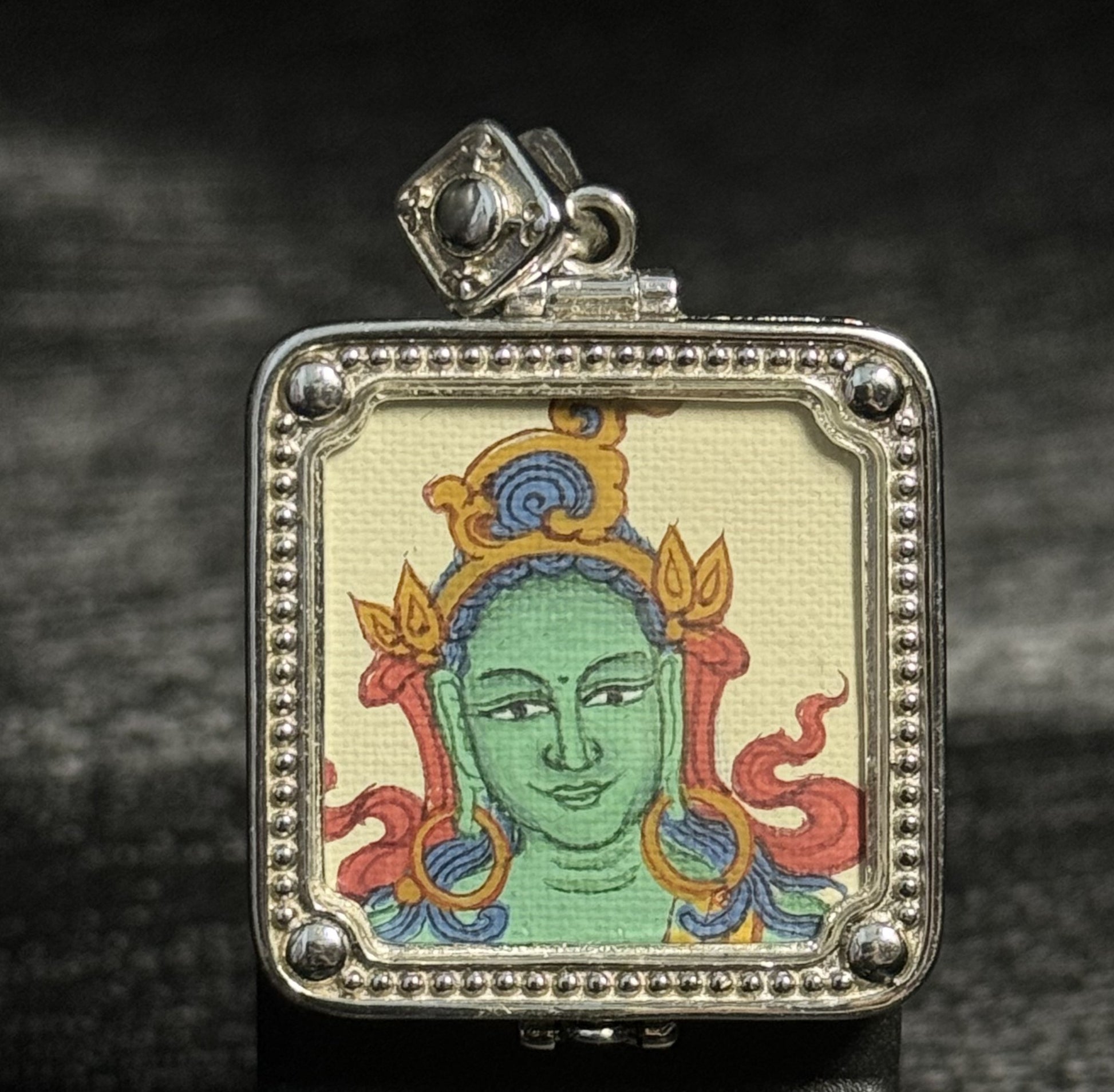 A 2x2cm hand-painted Tibet Green Tara Thangka pendant featuring the Tara Who Rescues from Eight Perils, representing rescue and wisdom in Buddhist tradition.
