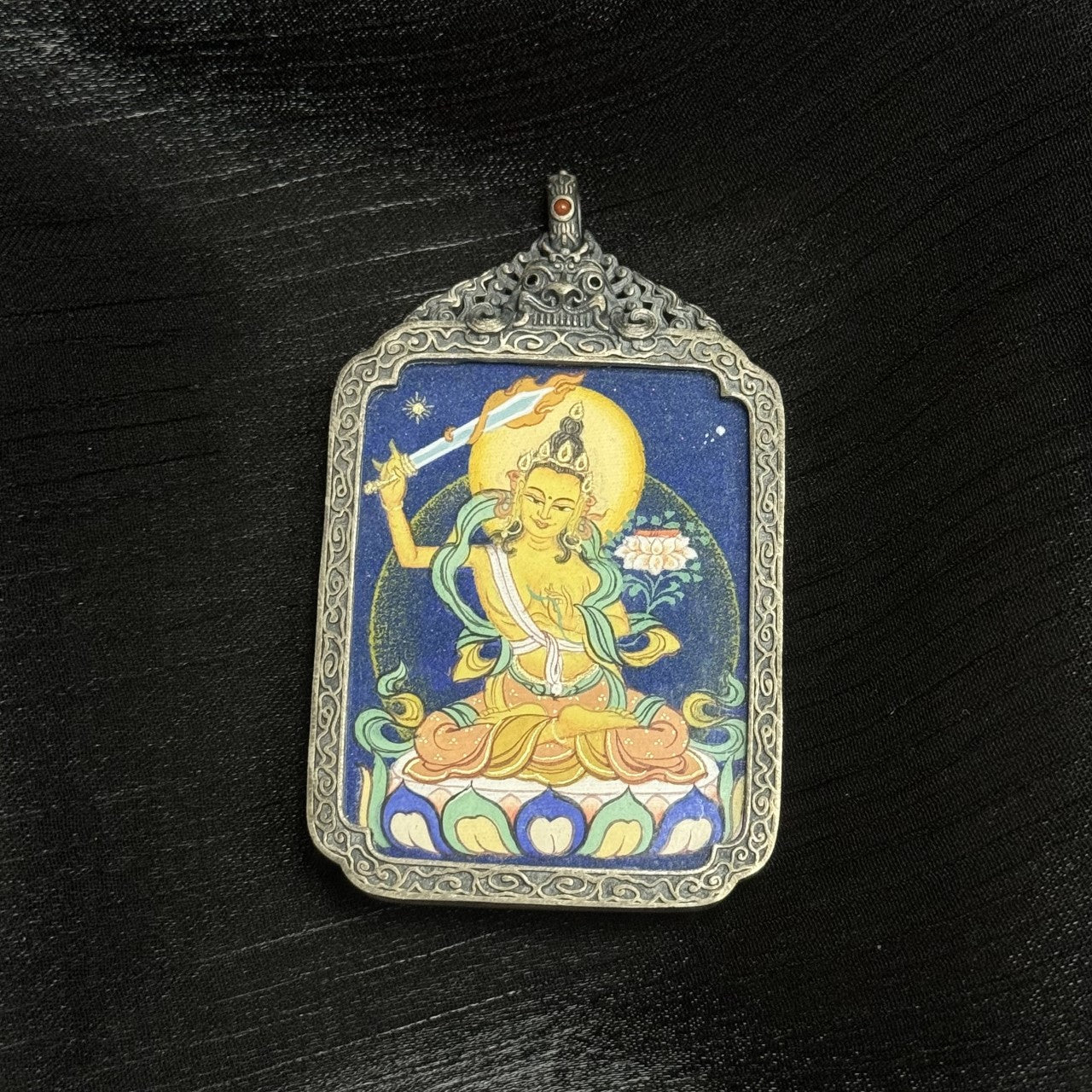  Detailed view of the antique silver-tone casing for the Manjushri Thangka pendant, symbolising protection and elegance in Tibetan Buddhist tradition.

