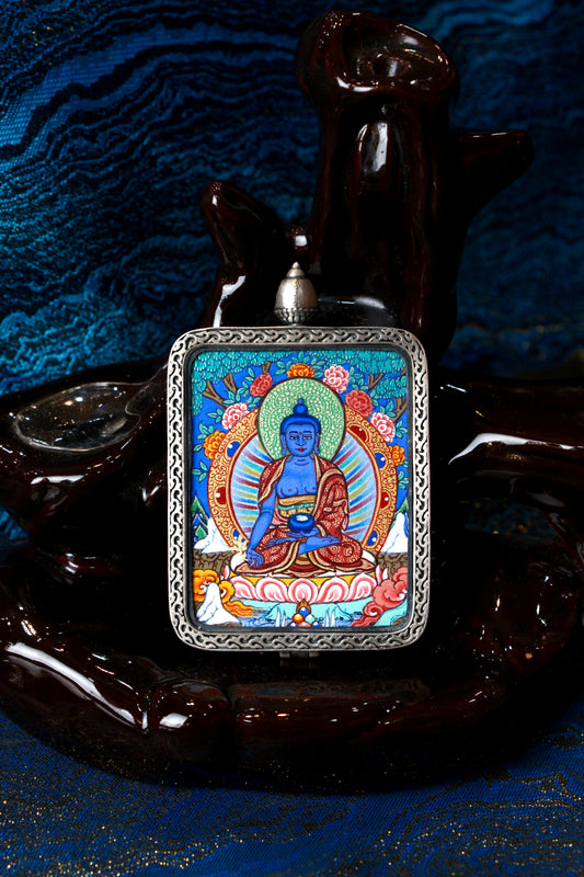 A sacred hand-painted Medicine Buddha Thangka pendant from Regong, featuring the blue deity of healing in a fine silver frame.