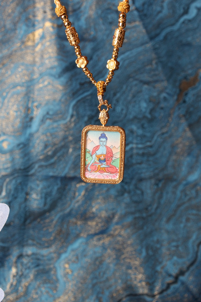 The Tibetan Buddhist Medicine Buddha Thangka pendant displayed as a sacred amulet for healing and longevity, embodying the compassionate healing power of Tibetan Buddhist tradition.
