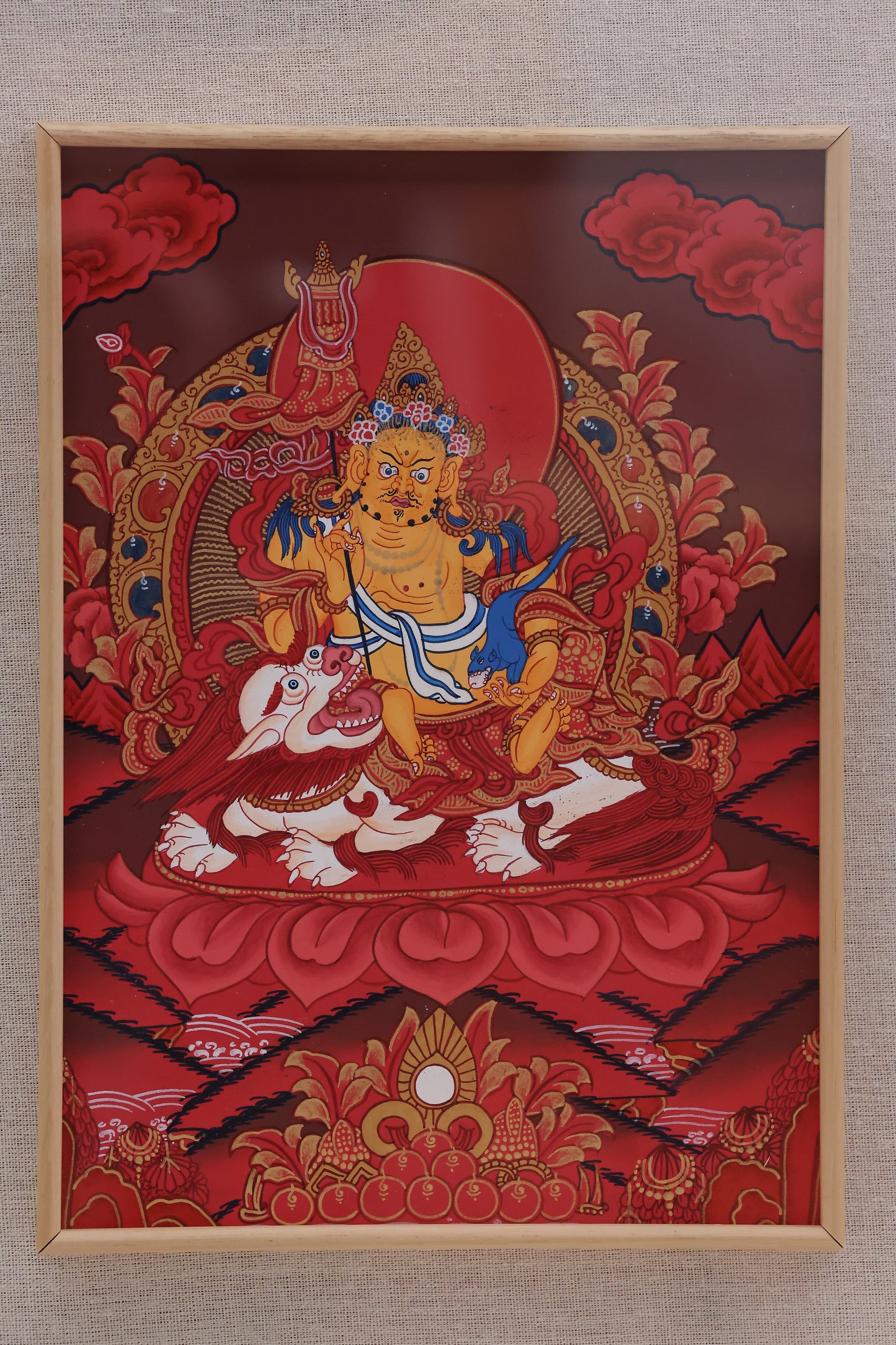Alt: Cai Bao Tian Wang depicted in a red Thangka painting, traditional Tibetan style.
