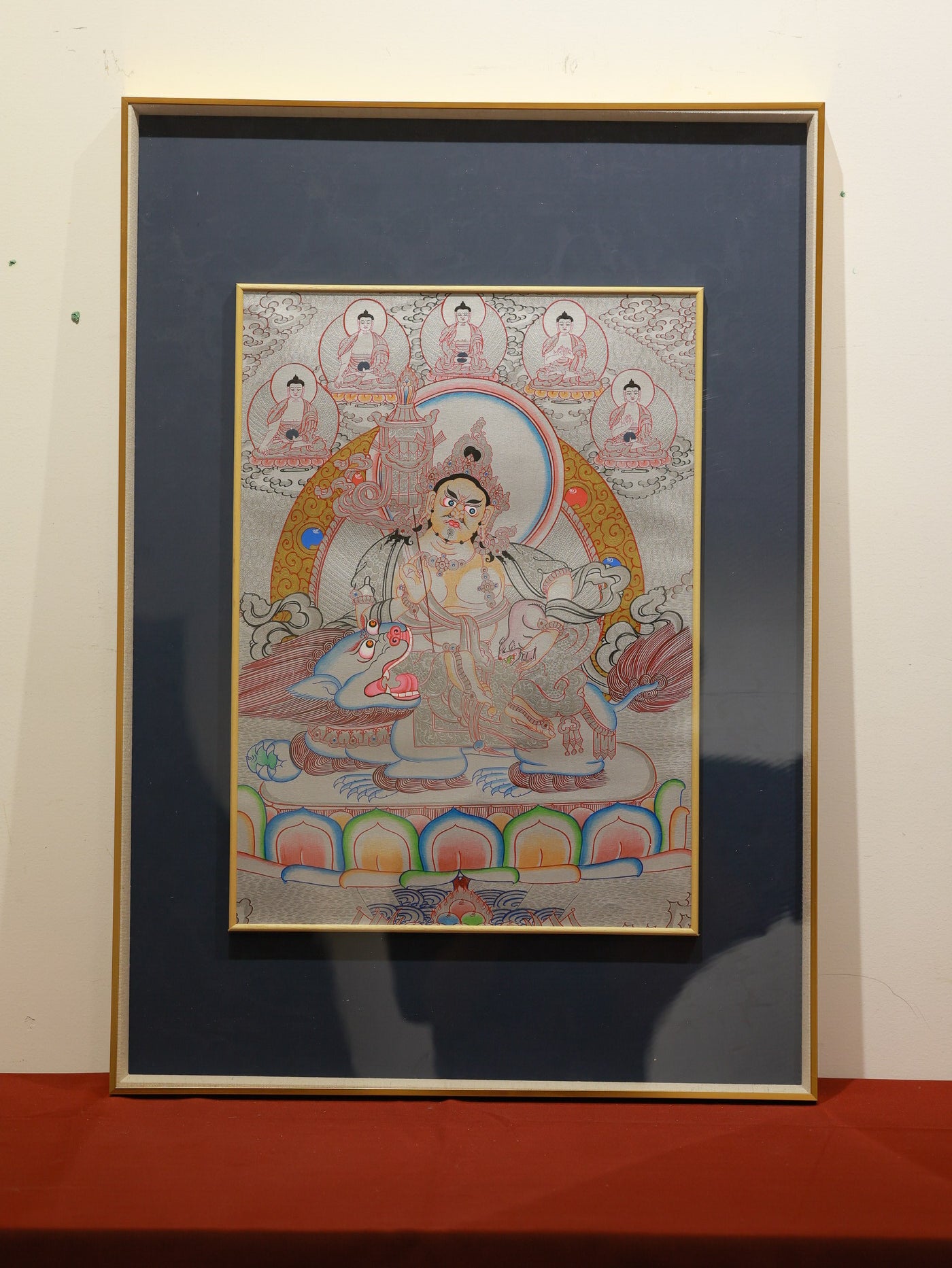 Silver-thangka of Vaishravana riding snow lion mount, holding jewel-spitting mongoose and treasure umbrella, detailed silver pigment on traditional canvas.