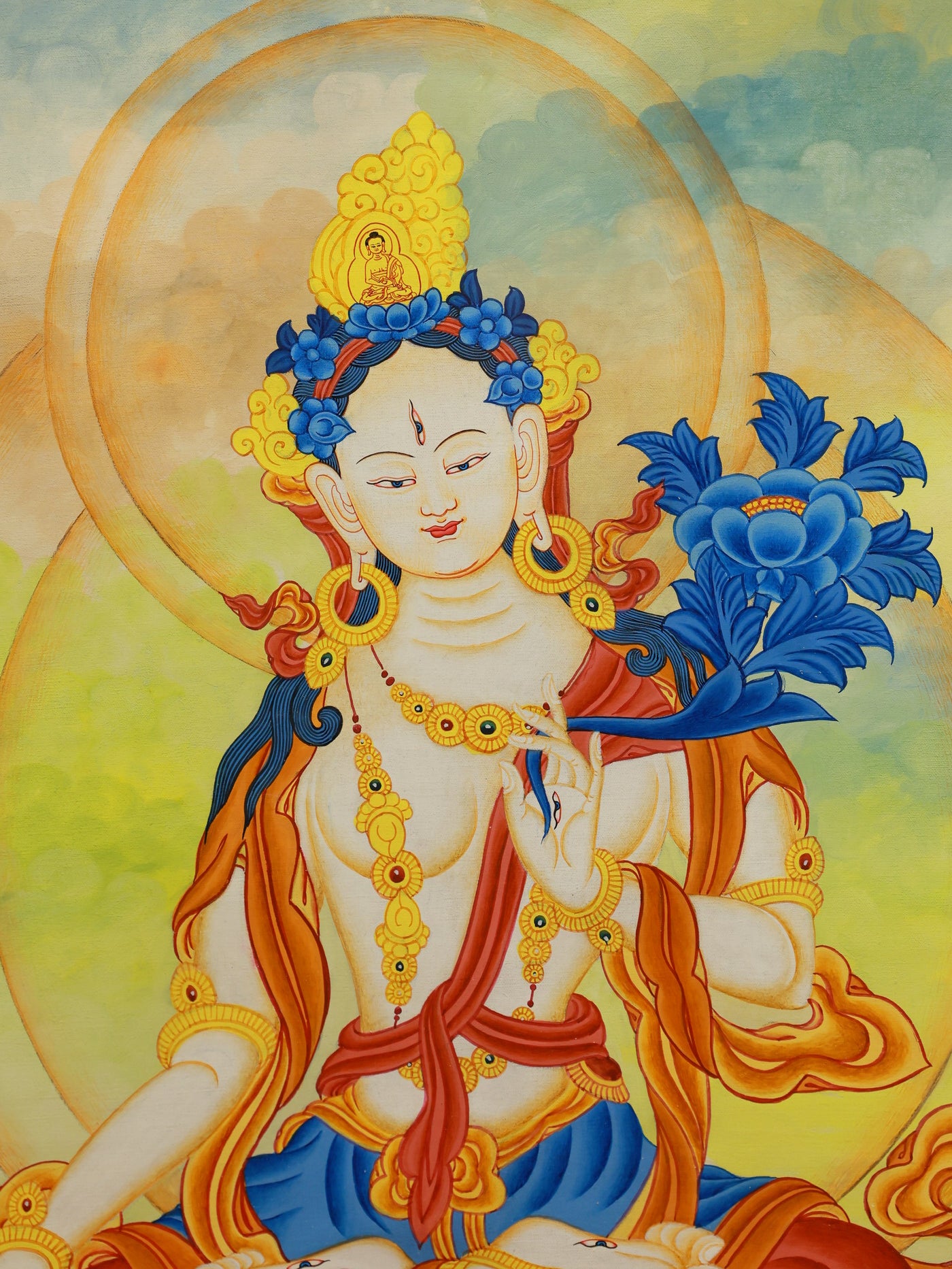 Color thangka of White Tara forming a gesture of compassion. Her third eye (urna) signifies wisdom, while she gently holds the stems of blossoming lotuses, symbols of purity and enlightenment.