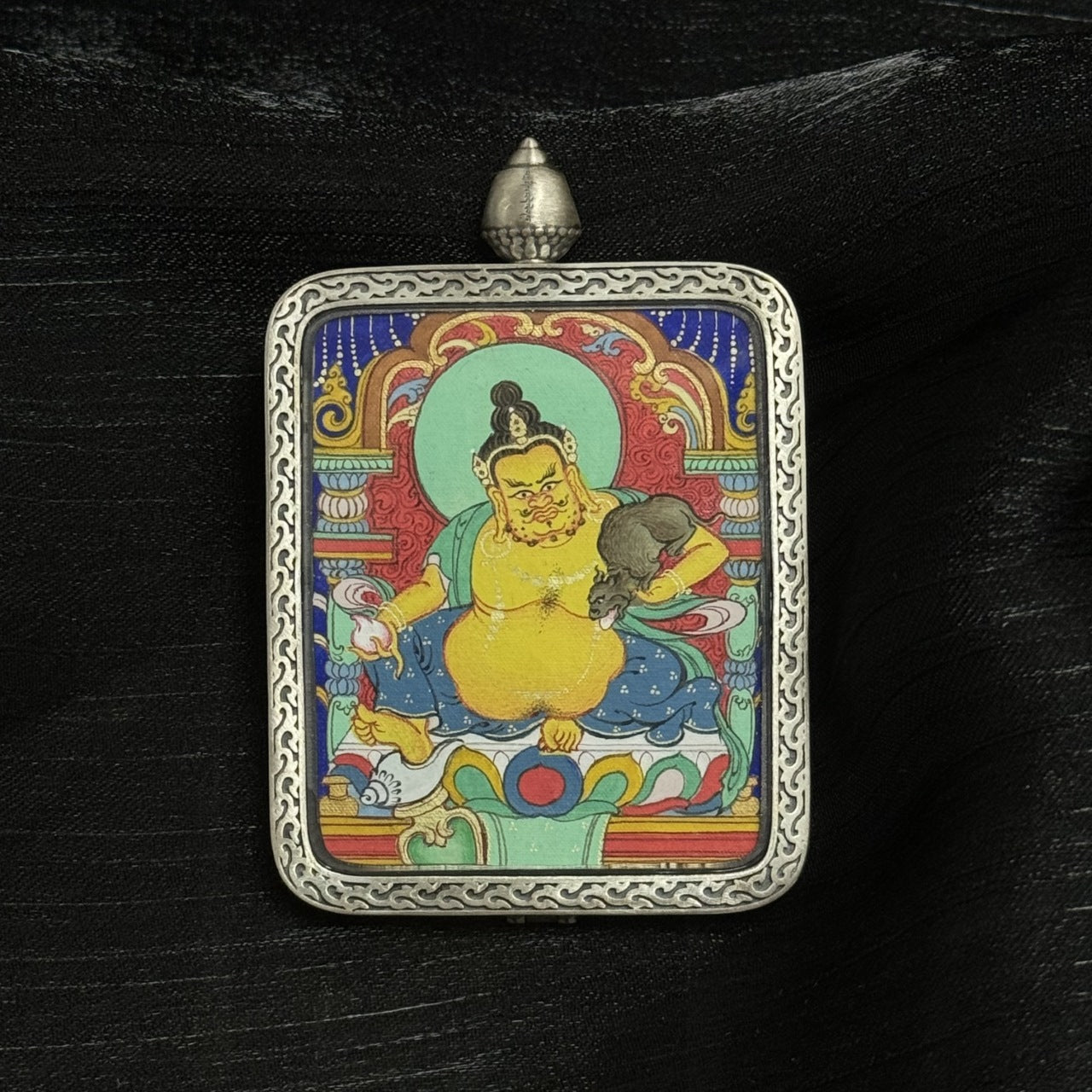 The Chigung Yellow Jambhala Thangka pendant displayed as a sacred amulet for wealth and merit, embodying the king of wealth deities in Tibetan Buddhist tradition.

