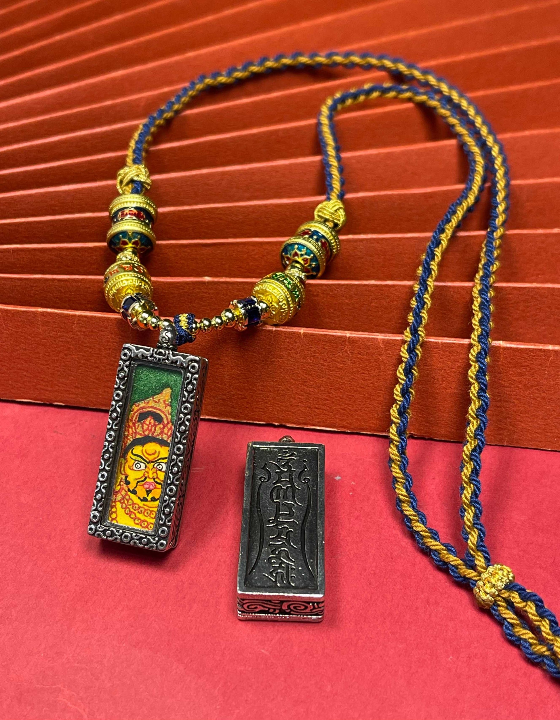  The Nepal Green Base Bold Yellow Jambhala Thangka pendant with silver copper casing displayed as a sacred amulet for prosperity, embodying Buddhist tradition.

