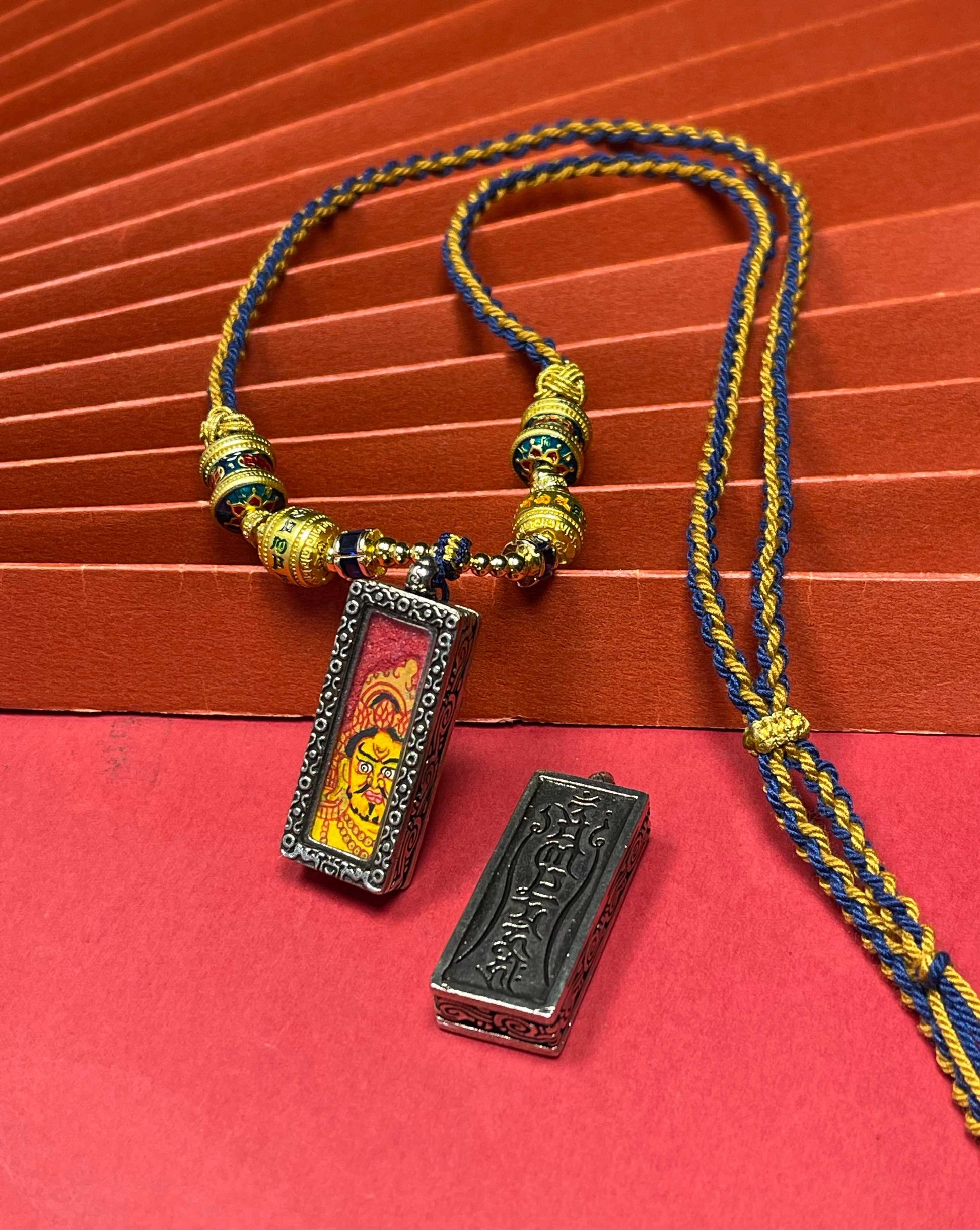  The Nepal Red Base Bold Yellow Jambhala Thangka pendant with silver copper casing displayed as a sacred amulet for prosperity, embodying Buddhist tradition.
