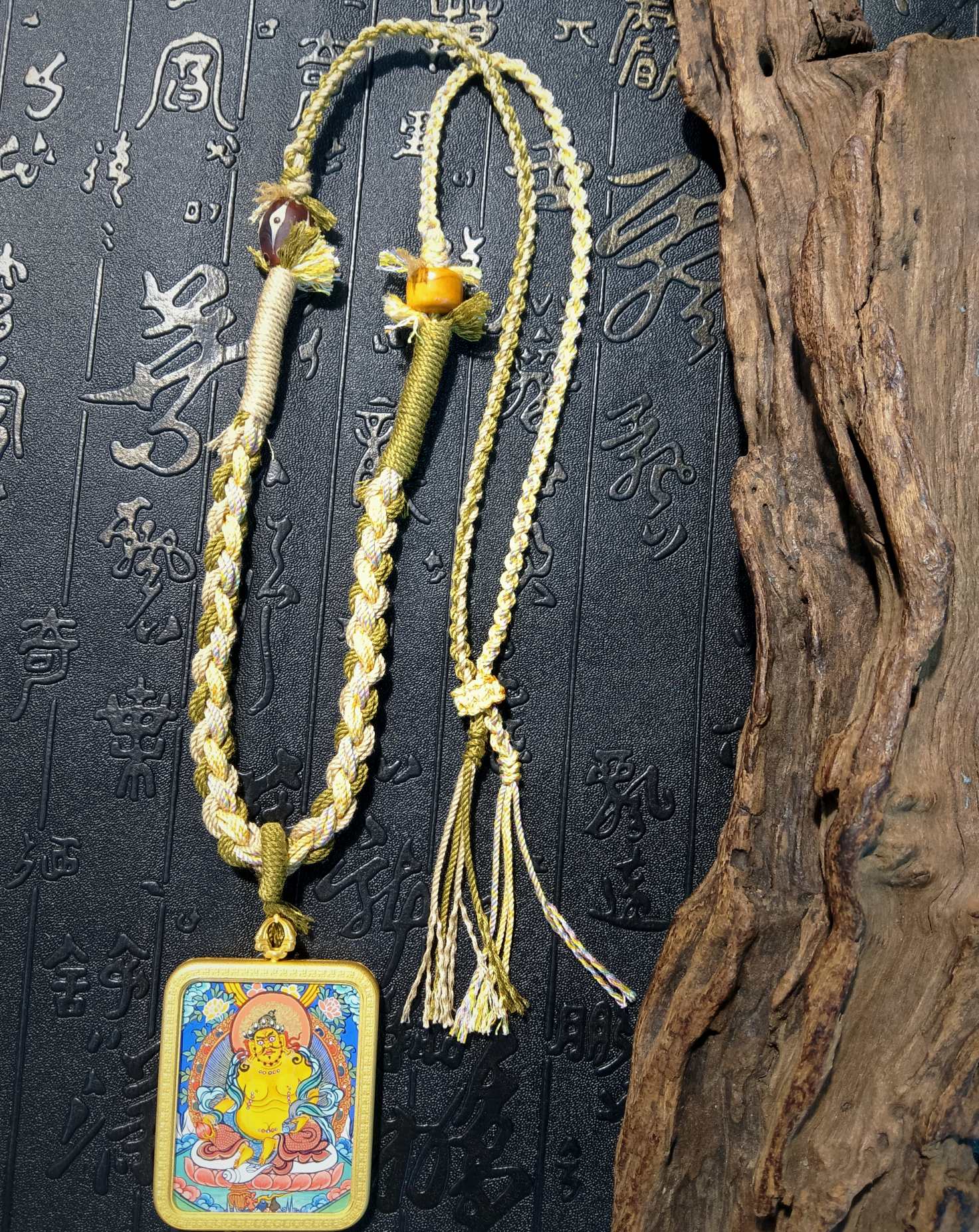  The Rekong Yellow Jambhala 3.5x4.5cm pendant with frosted copper and glass cord displayed as a necklace for wealth and career.
