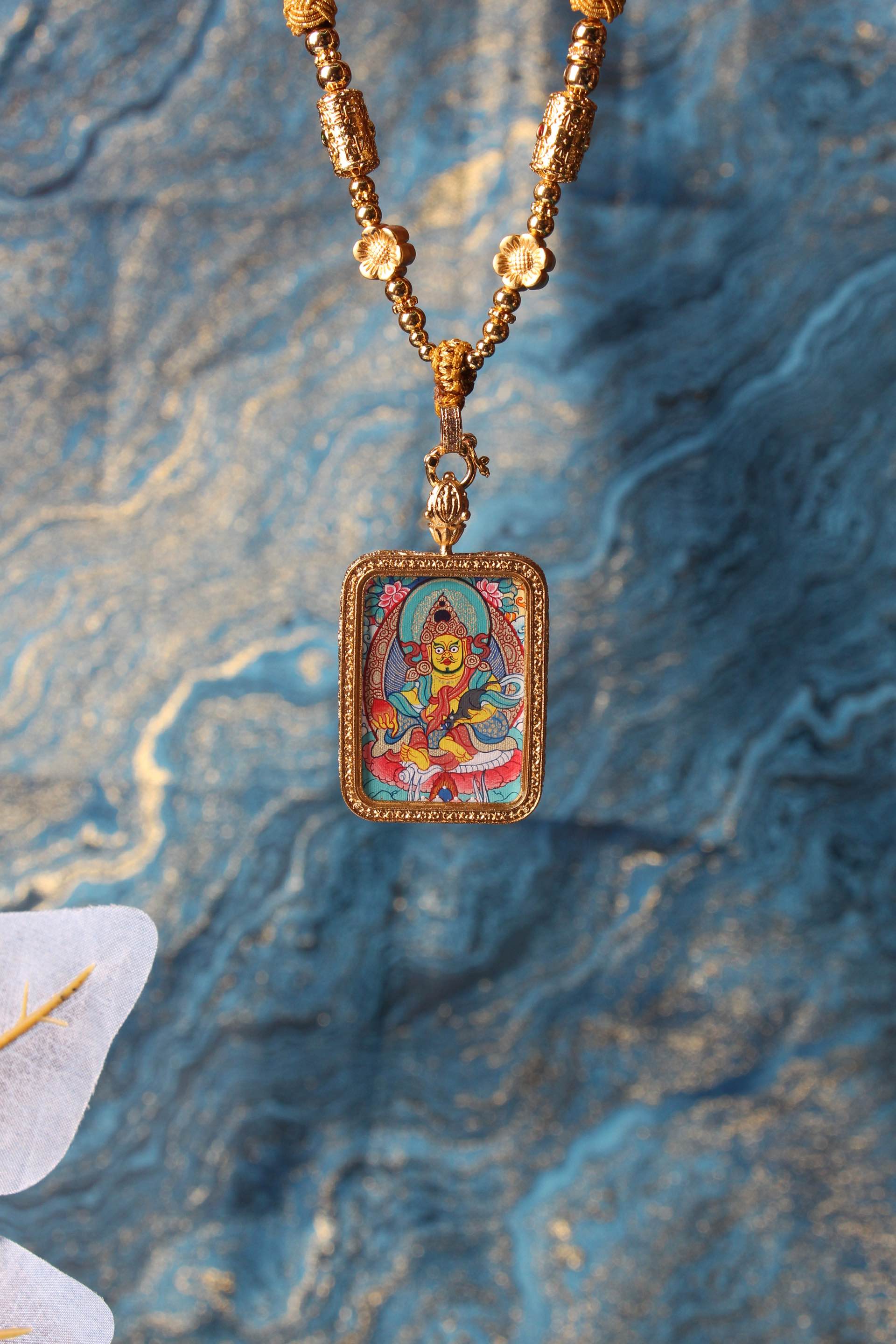 The Tibetan Buddhist Yellow Jambhala Thangka pendant displayed as a sacred amulet for wealth and prosperity, embodying the blessing of abundance in Tibetan Buddhist tradition.
