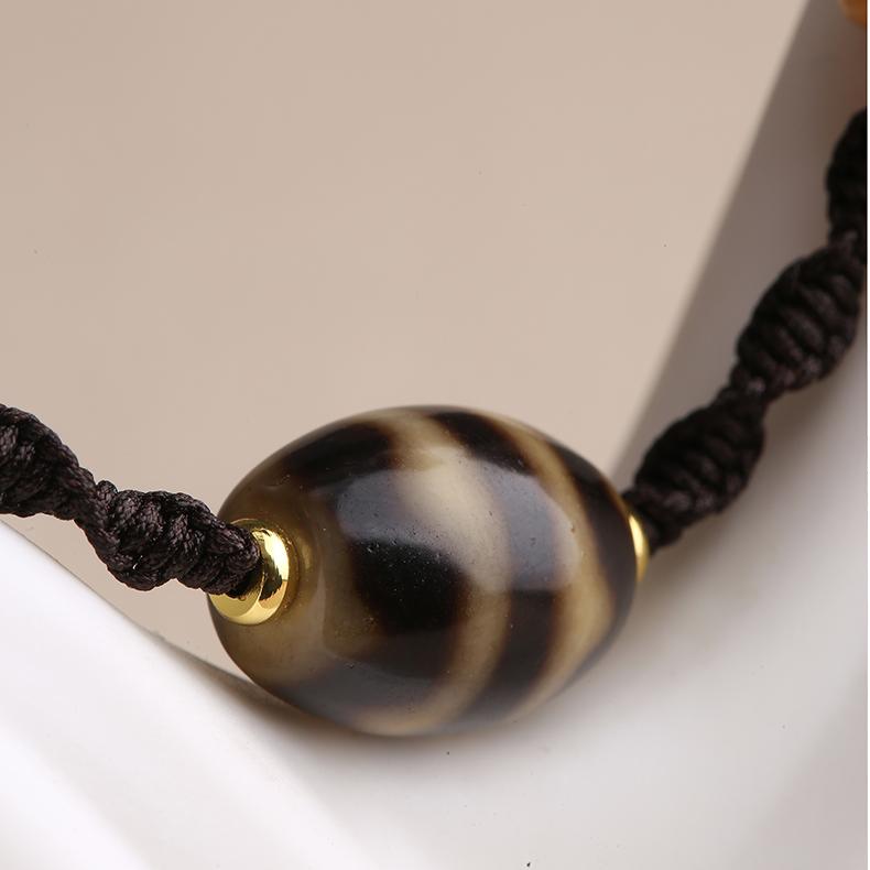 Handcrafted Dzi bead pendant with tiger tooth pattern and natural bone craftsmanship.