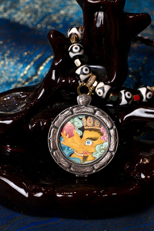 A sacred hand-painted Yellow Jambhala side profile Thangka pendant from Tibet, featuring the Wealth God with a Ruyi treasure in a silver Three Rabbits case.